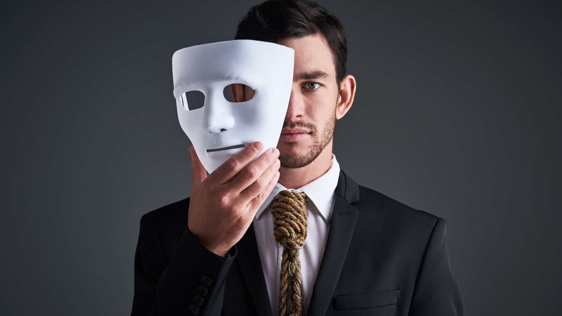 Two faces, holding mask and businessman portrait in a studio with serious face with secret and fraud. Worker or corporate criminal with rope tie showing identity theft or liar in business suit mockup